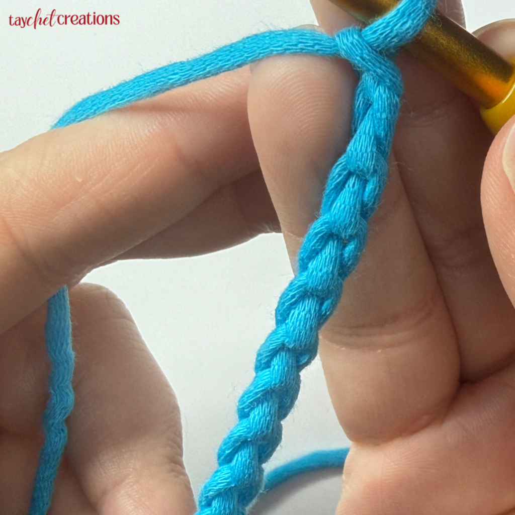 This image shows a set of hands holding a crochet hook and a chain showing the back of the chain 